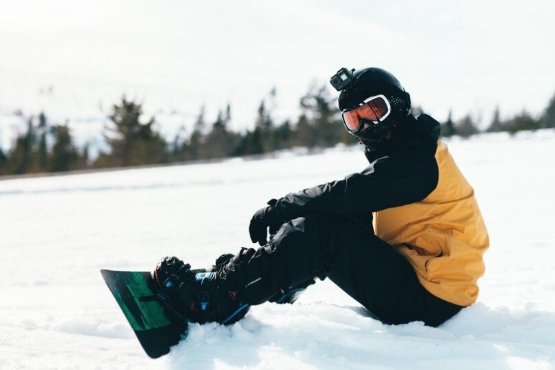 A snow skier wearing all skiing gear sitting on snow.