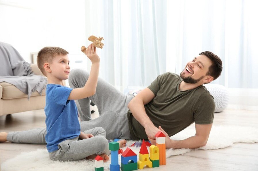 A smiling father playing with his child in room